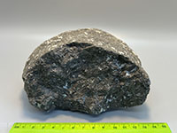 A dark, crystalline rock composed mostly of fiberous-appearing layered crystals of hornblende with some white speckles of feldspar.